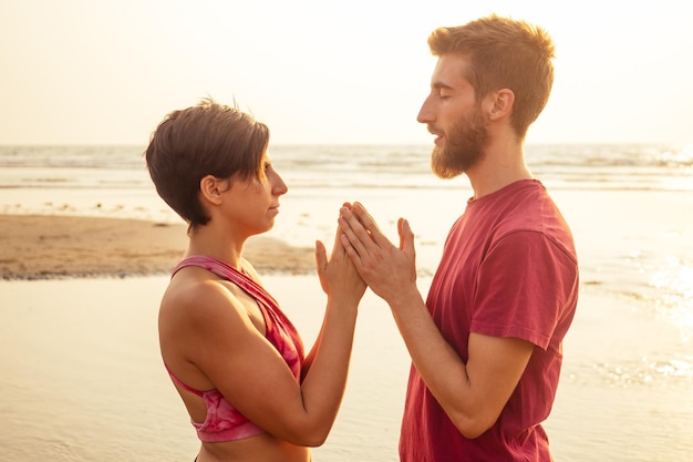 Photo muladhara swadhisthana manipula tantra yoga sur la plage homme et femme médite assis sur le sable au bord de la mer au coucher du soleil romantique saint valentin couple pratiquant le yoga vapeur