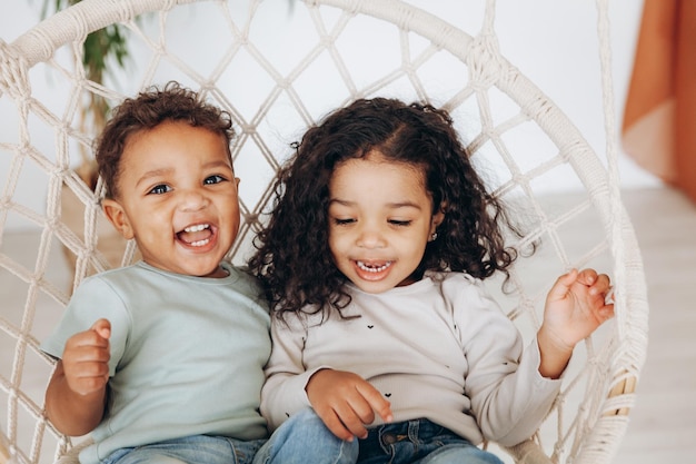 Photo mulâtres à la peau sombre un garçon et une fille sont assis dans un fauteuil suspendu en osier et font du vélo les enfants s'aiment et s'embrassent