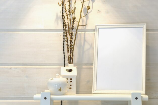 Mur blanc en bois dans une maison scandinave, maquette d'un cadre photo blanc sur une étagère, fleurs sèches. Intérieur scandinave.