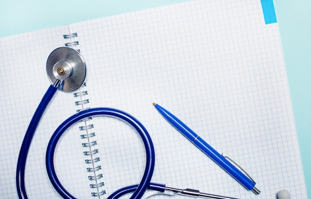 Sur un mur bleu clair, un cahier vierge ouvert, un stylo bleu et un stéthoscope. Place pour insérer du texte. Vue d'en-haut. Concept médical