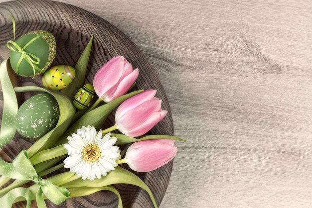 Mur en bois de Pâques avec des oeufs peints et des fleurs de printemps