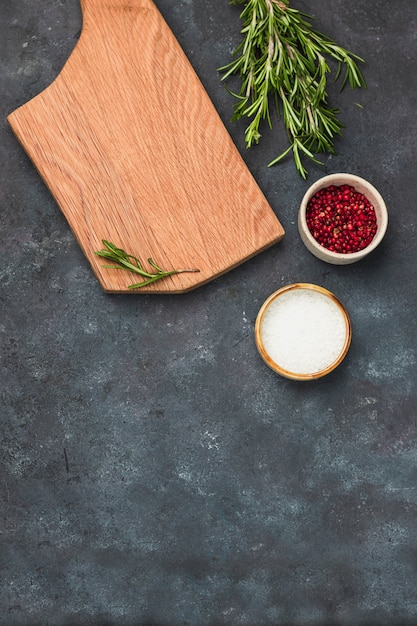 Mur culinaire. planche à découper en bois, romarin, sel de mer et poivre rose sur une table de cuisine en pierre grise. mise à plat avec espace de copie.