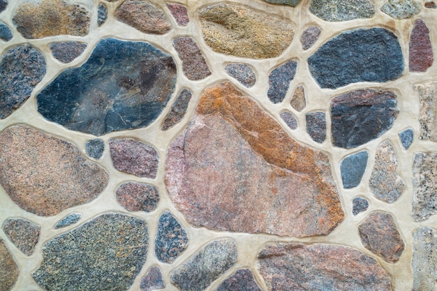 Le mur est fait de pierre naturelle et de ciment. Fragment d'un mur de pierre coloré et texturé. Brillant