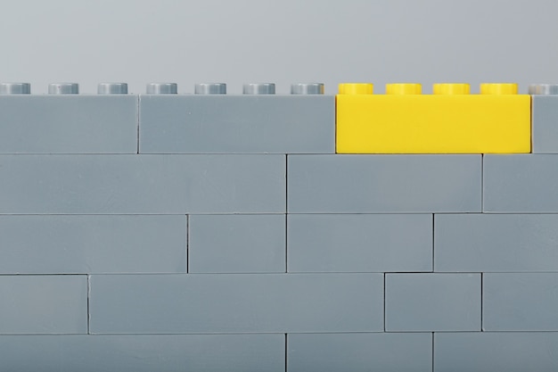 Un mur gris fait d'un jeu de construction jouet avec la dernière brique jaune