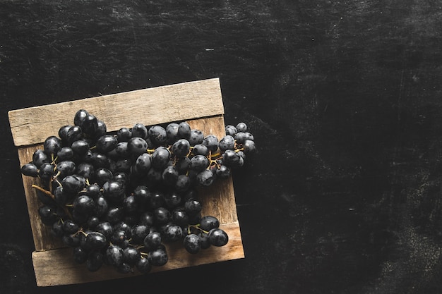 Sur un mur gris un raisin sombre dans une boîte en bois