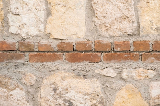 Mur de grosses pierres calcaires et de béton et une bande de briques rouges en arrière-plan