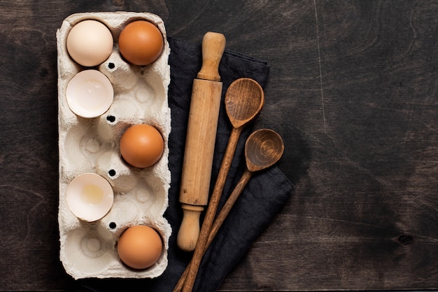 Mur de pâtisserie et culinaire. Oeufs de poule multicolores et coquilles dans un vieux récipient vintage en cellulose avec farine, sucre, cuillères en bois et un rouleau à pâtisserie sur le vieux mur en bois sombre. Vue de dessus.