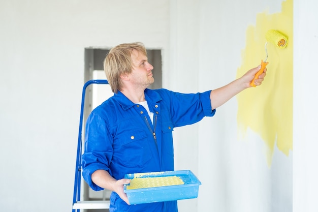 Mur de peinture d'homme de couleur jaune avec rouleau. Concept de rénovation, réparation et redécoration.