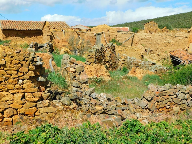 Un mur de pierre dans un village avec un champ d'herbe verte et une maison en arrière-plan.