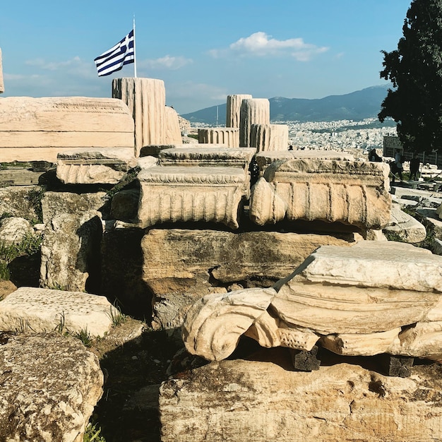 Mur de pierre par des rochers sur le rivage contre le ciel et le drapeau grec agitant dans les airs