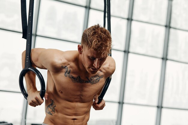 Muscleup exercice jeune homme faisant de l'entraînement croisé intense à la salle de sport sur des anneaux de gymnastique