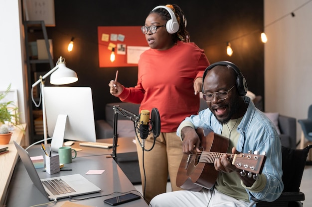 Musicien africain assis devant le microphone jouant de la guitare et chantant une chanson avec une femme pendant la diffusion en ligne