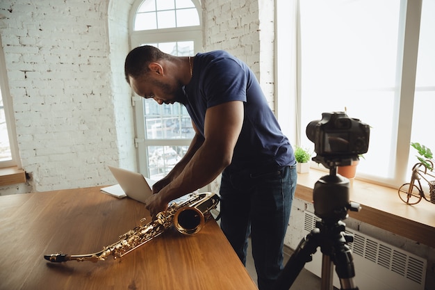 Musicien afro-américain jouant du saxophone lors d'un concert en ligne à la maison isolé et mis en quarantaine, attentionné, concentré