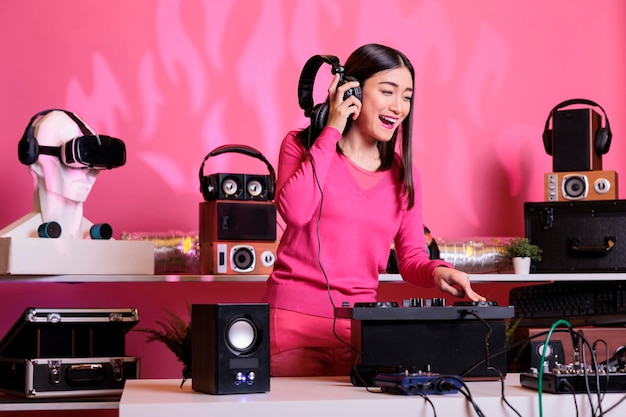 Musicien asiatique avec un casque jouant une chanson électronique à la console de mixage, debout à la table de dj s'amusant avec les fans la nuit dans le club. Artiste jouant de la musique techno en studio sur fond rose