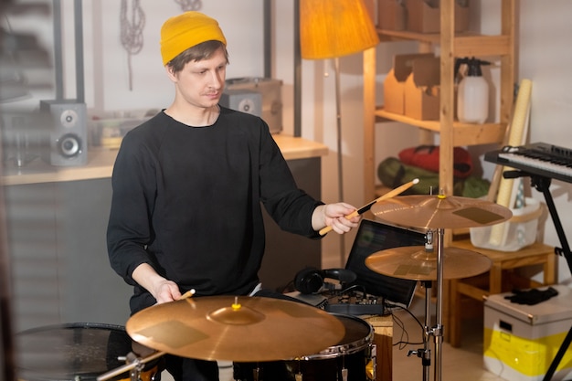 Musicien Contemporain En Tenue Décontractée Battant Des Cymbales Avec Des Baguettes En Bois Tout En Répétant Par Kit De Batterie Dans Le Garage