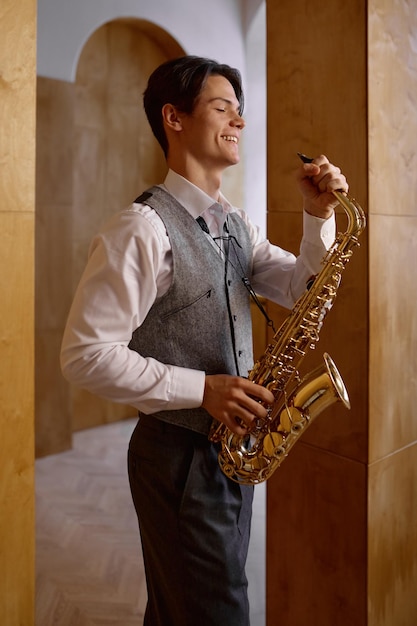 Musicien de jazz jouant du saxophone et appuyé contre le mur du studio d'art. S'entraîner avant la représentation