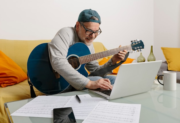 Musicien jouant de la guitare et composant de la musique avec ses collègues par vidéoconférence via son ordinateur portable