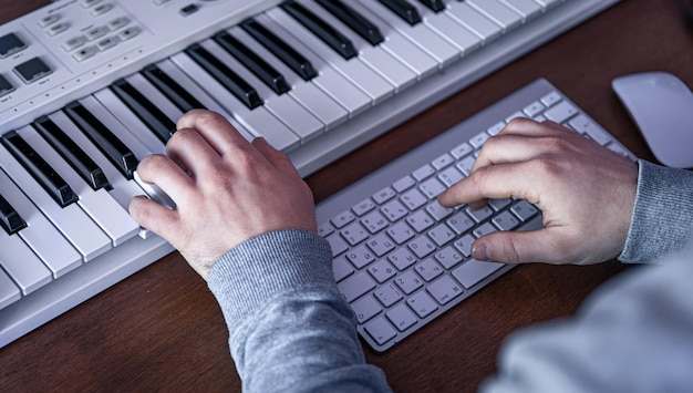 Un musicien masculin crée de la musique à l'aide d'un ordinateur et d'un clavier sur le lieu de travail d'un musicien