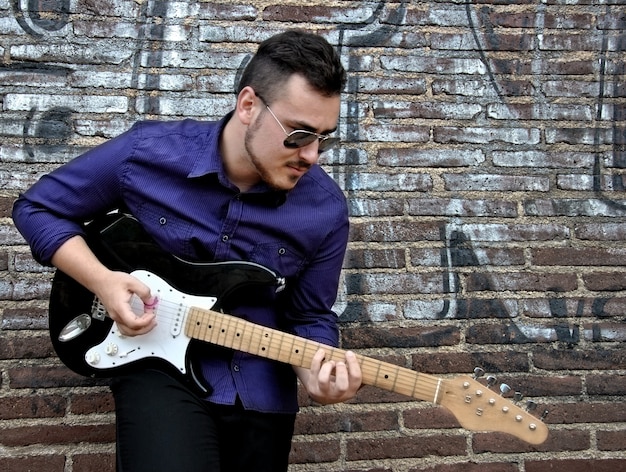 Musicien posant avec sa guitare dans un mur de graffitis