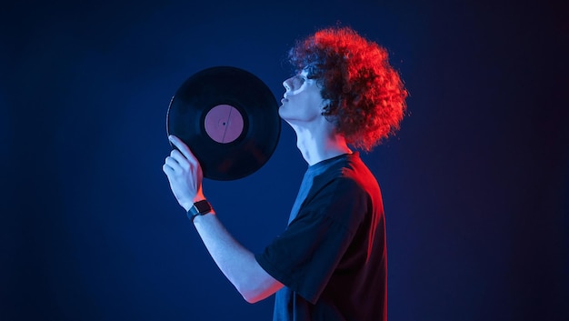 Musicien tenant du vinyle Jeune homme aux cheveux bouclés est à l'intérieur éclairé par un éclairage au néon