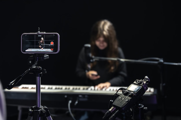 Une Musicienne Enregistrant Une Vidéo Sur Un Smartphone Debout Sur Un Trépied, à L'aide D'un Microphone Professionnel, D'un Blogueur Ou D'un Cours De Tir De Professeur De Musique En Studio, Assise Au Piano.