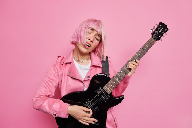 Une musicienne insouciante incline la tête chante la chanson préférée joue de la guitare électrique se produit sur scène étant la rock star populaire jas les cheveux roses à la mode posent à l'intérieur. Concept d'entreprise de spectacle de style de vie de musique