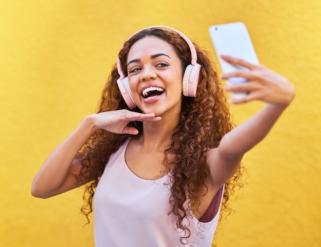 Musique femme noire heureuse et écouteurs pour selfie sur fond de mur jaune Visage d'une personne de la génération z avec un sourire en plein air pour écouter ou diffuser de l'audio de motivation pour un poste d'influenceur en Colombie