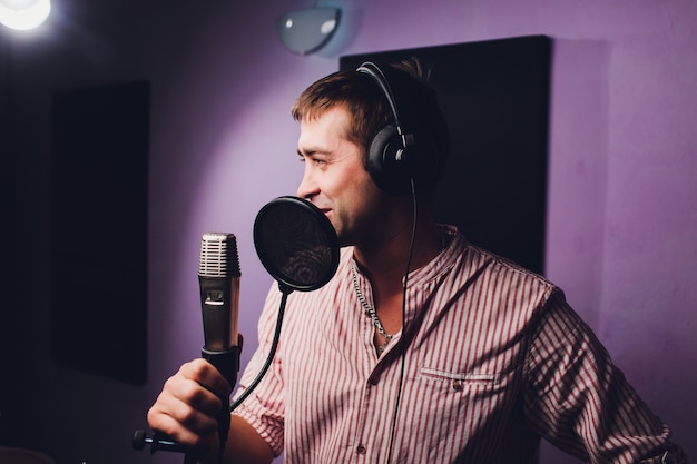 Musique, show-business, personnes et concept de voix - chanteur avec casque et microphone chantant une chanson au studio d'enregistrement sonore.