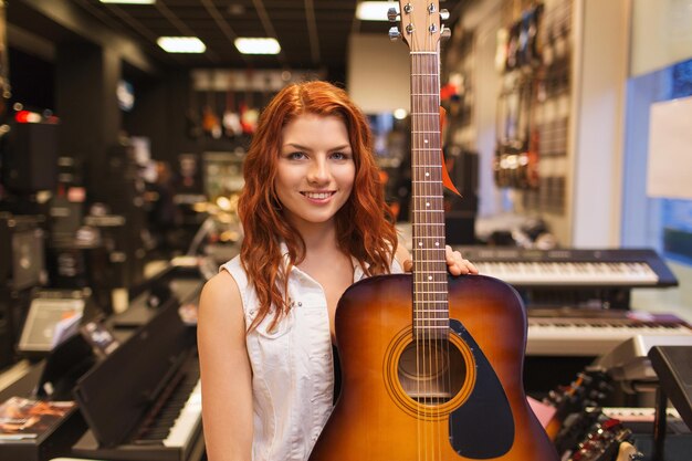 musique, vente, personnes, instruments de musique et concept de divertissement - assistante souriante ou cliente tenant une guitare acoustique dans un magasin de musique