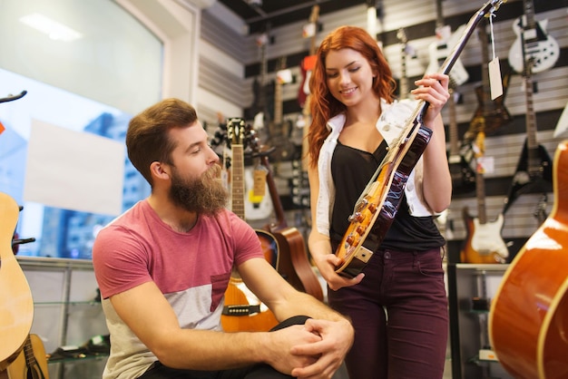 musique, vente, personnes, instruments de musique et concept de divertissement - couple heureux de musiciens avec guitare au magasin de musique