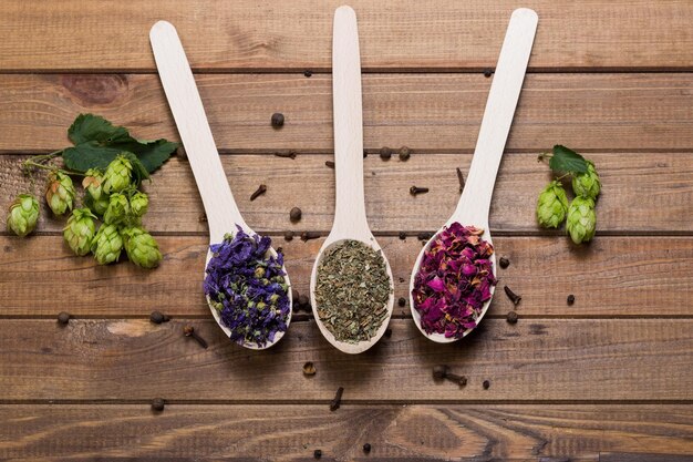 Photo myosotis séchés tisane de fleurs de mauve thé vert et fleurs de rose sur une cuillère sur une table en bois avec vue de dessus de houblon