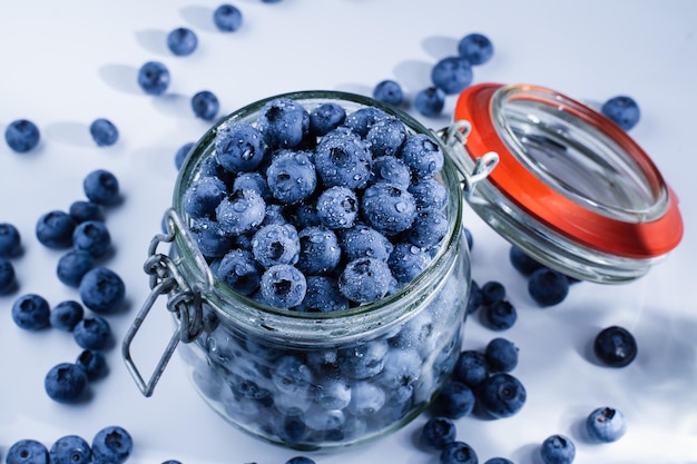 Myrtilles avec des gouttes d'eau dans un bocal en verre sur fond blanc Blueberry berry saisonnier d'été de nombreux bleuets biologiques naturels