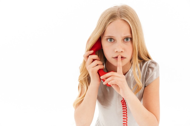 Mystère jeune fille blonde en robe parlant par téléphone tout en montrant le geste de silence sur blanc