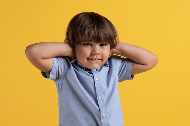 N'entendre aucun mal Agacé petit garçon couvrant les oreilles avec les mains et regardant l'arrière-plan studio orange de la caméra