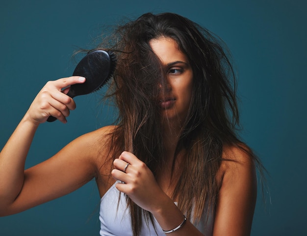 Ce n'est pas seulement une coiffure, c'est un état d'esprit Prise de vue en studio d'une belle jeune femme tenant une brosse à ses cheveux posant sur un fond bleu