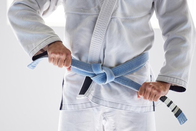 Ce n'est plus un amateur Photo recadrée d'un artiste martial masculin méconnaissable attachant sa ceinture dans la salle de sport