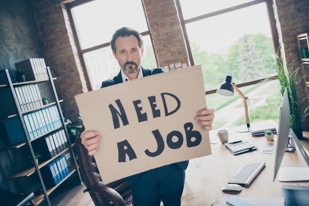 Ce n'est plus le patron. Photo de désespoir de mauvaise humeur triste licencié travailleur licencié mec mature tenir une affiche affiche recherche nouvel emploi dernier jour de travail lieu de travail congédié mauvaise humeur bureau moderne à l'intérieur