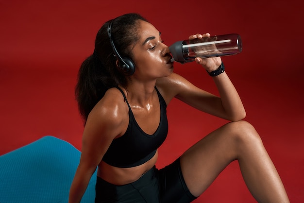 N'oubliez pas de boire assez d'eau épuisée belle et jeune femme en vêtements de sport tout en buvant de l'eau