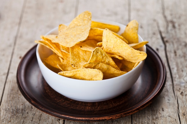 Nachos mexicains frites dans un bol blanc sur une plaque en céramique brune.