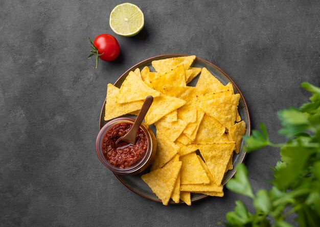 Nachos ou tortillas avec sauce tomate épicée sur une assiette avec des herbes fraîches sur fond sombre Croustilles de maïs avec sauce salsa Snack mexicain classique