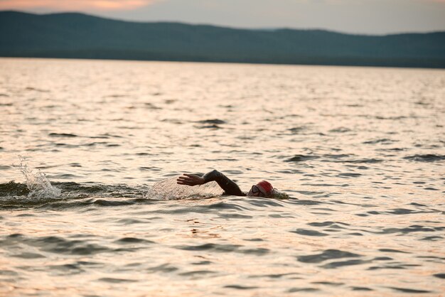 Nageur en maillot de bain nageant seul dans le lac pendant le coucher du soleil dans la nature