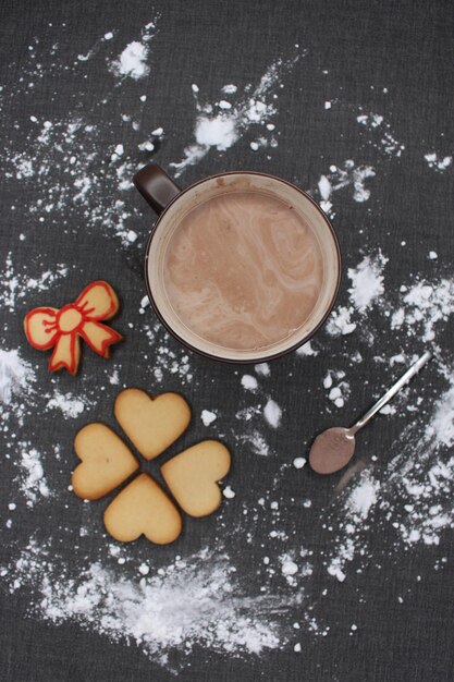 Photo une nappe noire avec de la farine une tasse de biscuits au chocolat chaud et une cuillère avec du cacao noël