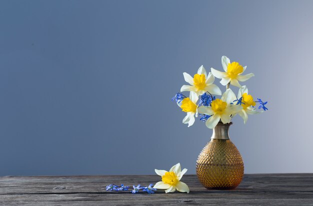 Narcisse jaune et perce-neige bleu dans un vase sur une table en bois sur une surface sombre