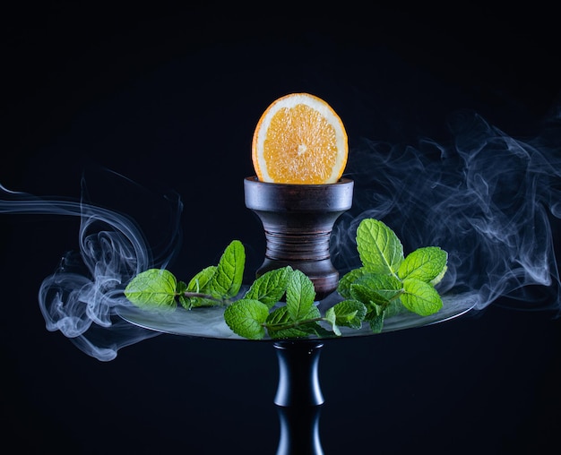 Narguilé aux fruits avec menthe orange tabac et fumée sur fond noir