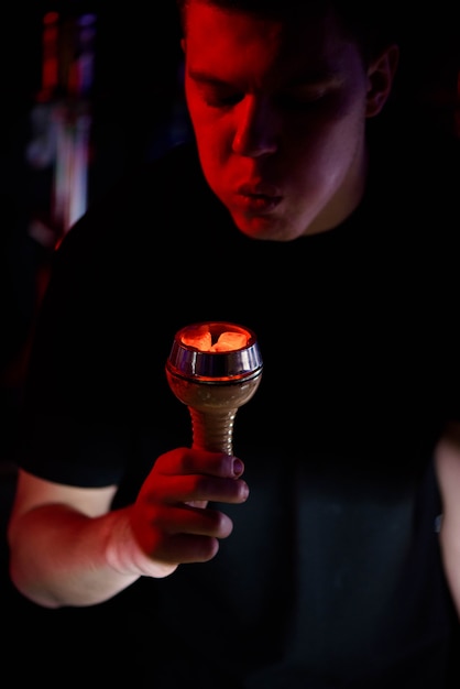 Narguilé Shisha, charbons ardents rouges. L&#39;homme souffle des braises pour voler des étincelles.