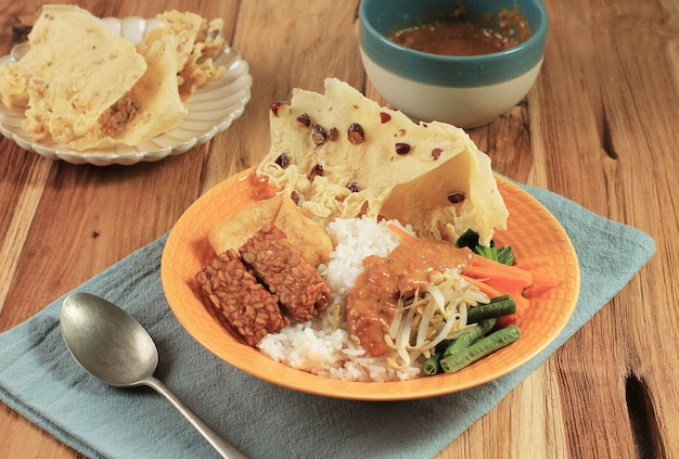 Nasi Pecel. Plat traditionnel de riz javanais composé de riz cuit à la vapeur avec salade de légumes, vinaigrette aux arachides, tempeh, tofu et craquelins.