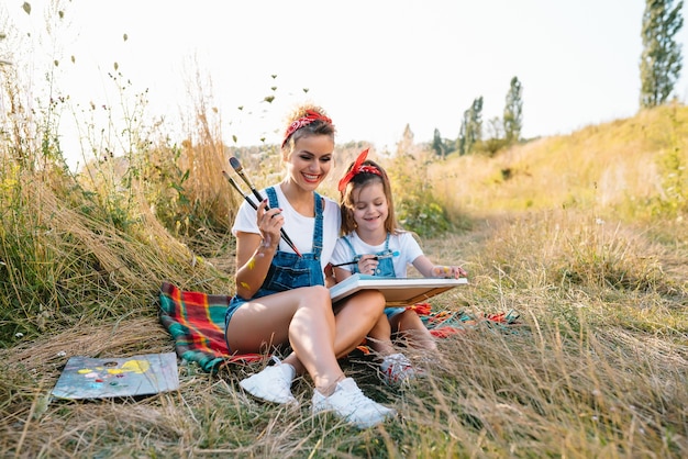 Nature ensoleillée, maman et fille peignent une image dans un parc, peignant un petit enfant, créativité enfantine.