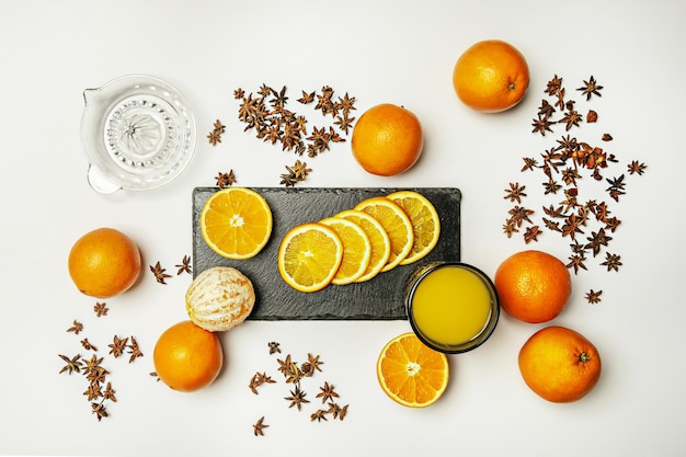 Photo nature morte aux agrumes avec de délicieuses tranches d'oranges entières pelées, un presse-agrumes et un verre de jus sur une surface blanche