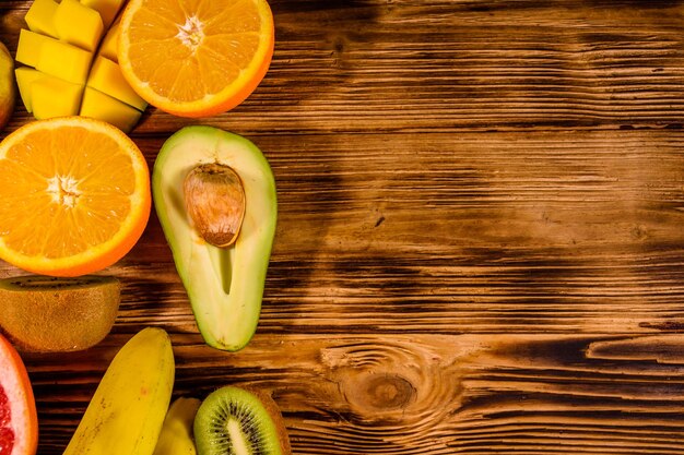 Nature morte aux fruits exotiques bananes mangue oranges avocat pamplemousse et kiwis sur table en bois vue de dessus