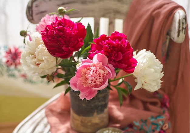 Nature morte aux pivoines blanches et roses dans un vieux vase en céramique sur chaise vintaje